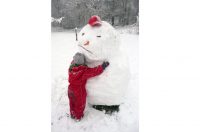 Barn i röd overall kramar en snögubbe med keps